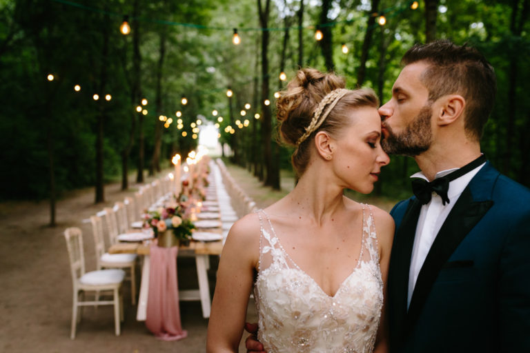 Lo sposo bacia la sposa sulla fronte davanti al tavolo per la cena di nozze